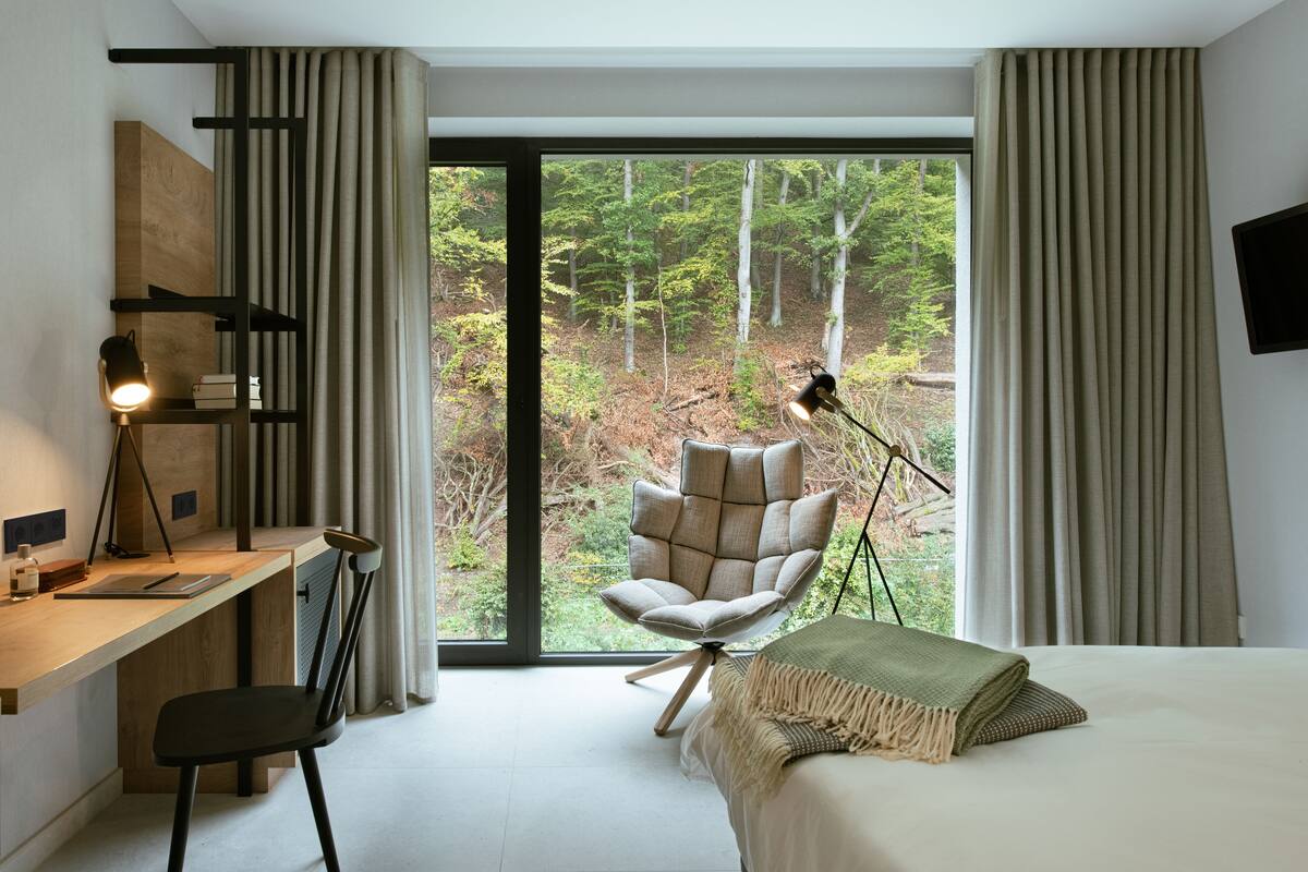 Un dormitorio moderno con una ventana grande, un escritorio, una silla, una cama y una lámpara de pie.