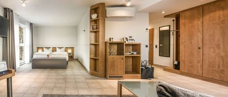 Una habitación de hotel moderna con una cama grande, una mesa de centro de vidrio, un sofá, un armario de madera y un guardarropa.