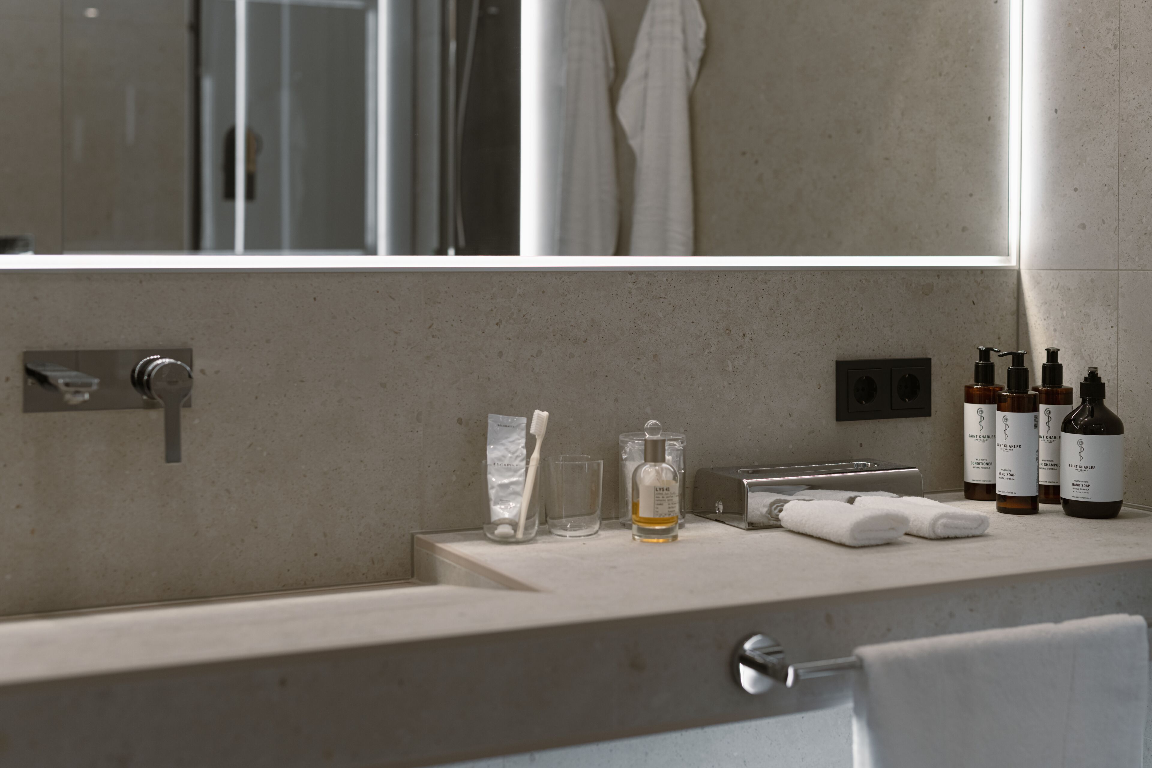 Un baño moderno con un espejo grande, un lavabo y distintos artículos de aseo.