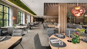 Un restaurante moderno con techo alto, ventanas amplias y una pared verde. Las mesas están dispuestas con vasos y cubiertos.