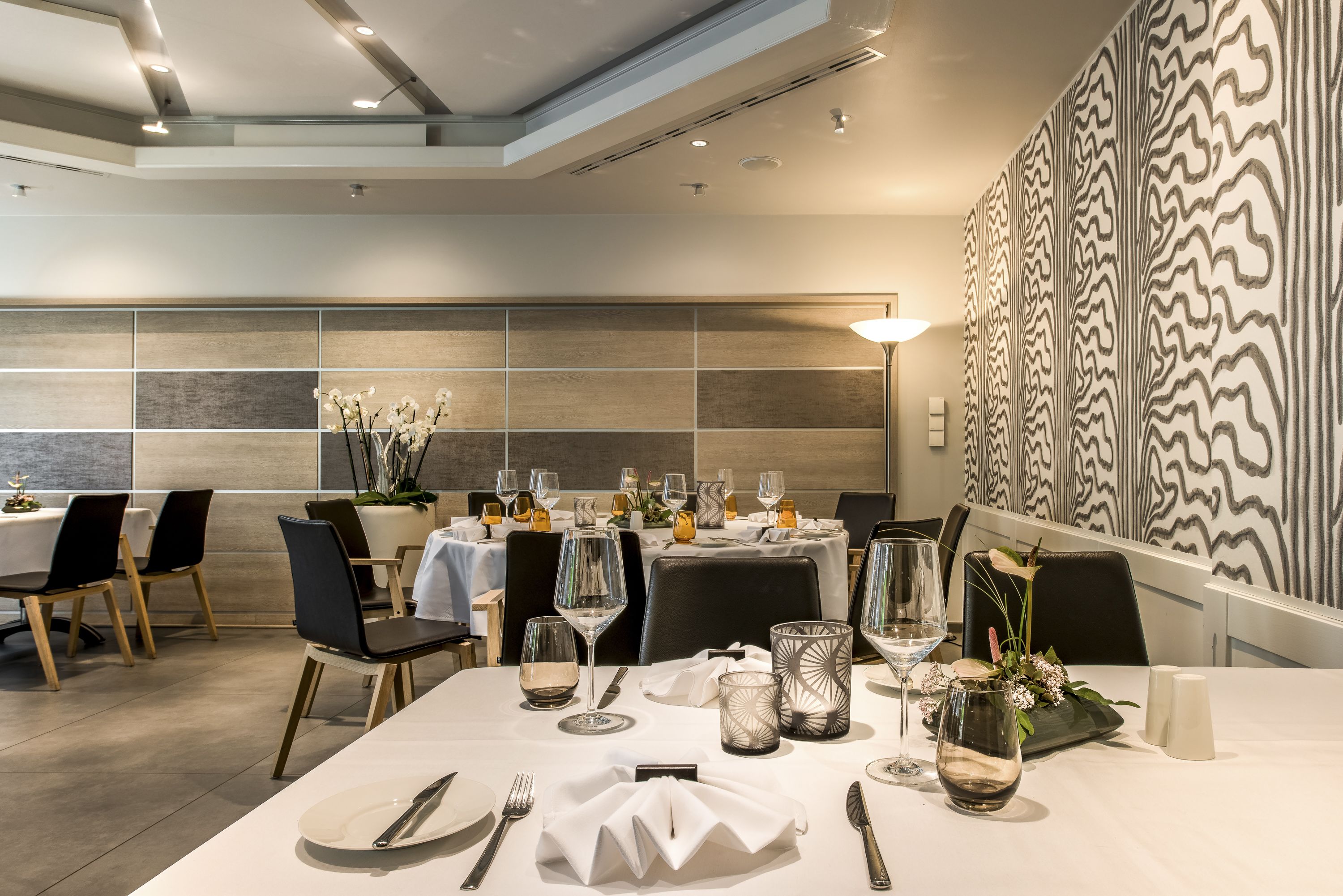 A dining area with tables set for a meal, featuring modern decor and a patterned wall in the background.