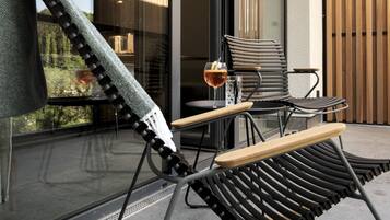 A modern outdoor seating area with a rocking chair and a table, a glass of drink, and a view of the interior through a glass door.
