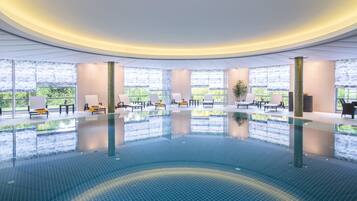 A modern indoor swimming pool with lounge chairs and large windows.