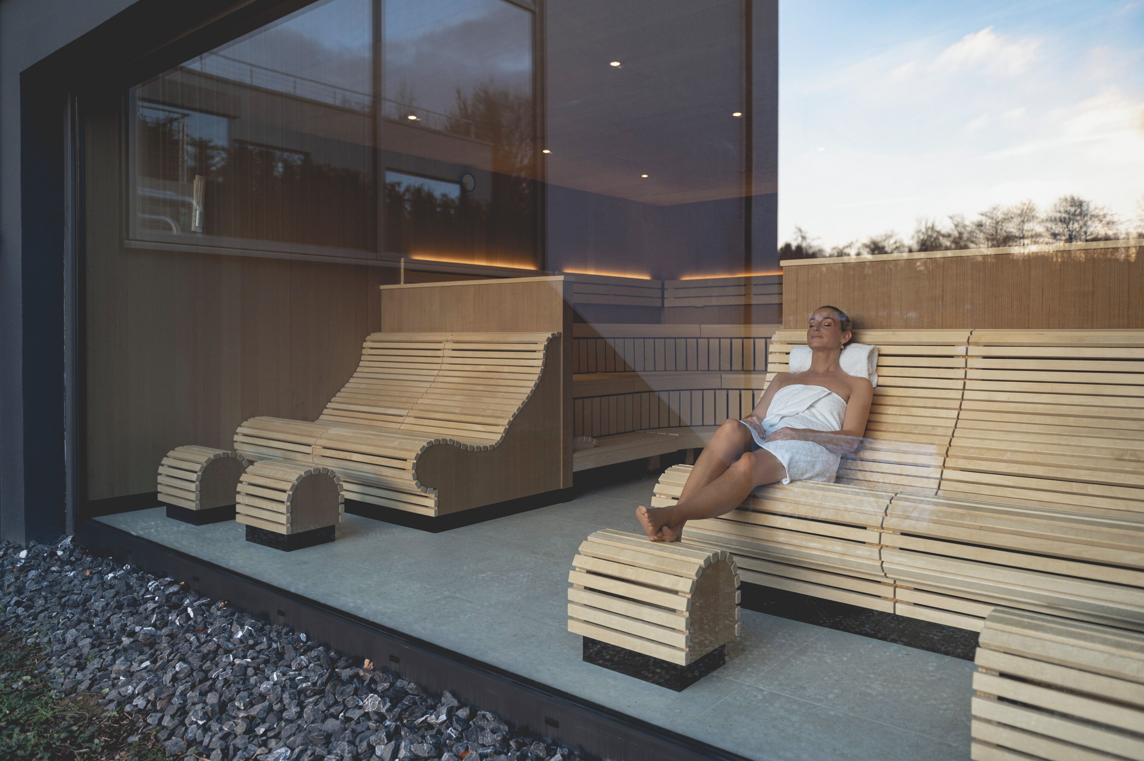 A modern outdoor seating area with wooden benches and a glass wall reflecting the sky.