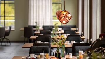 A restaurant with tables set for breakfast, including cups, bowls, and a vase with flowers.