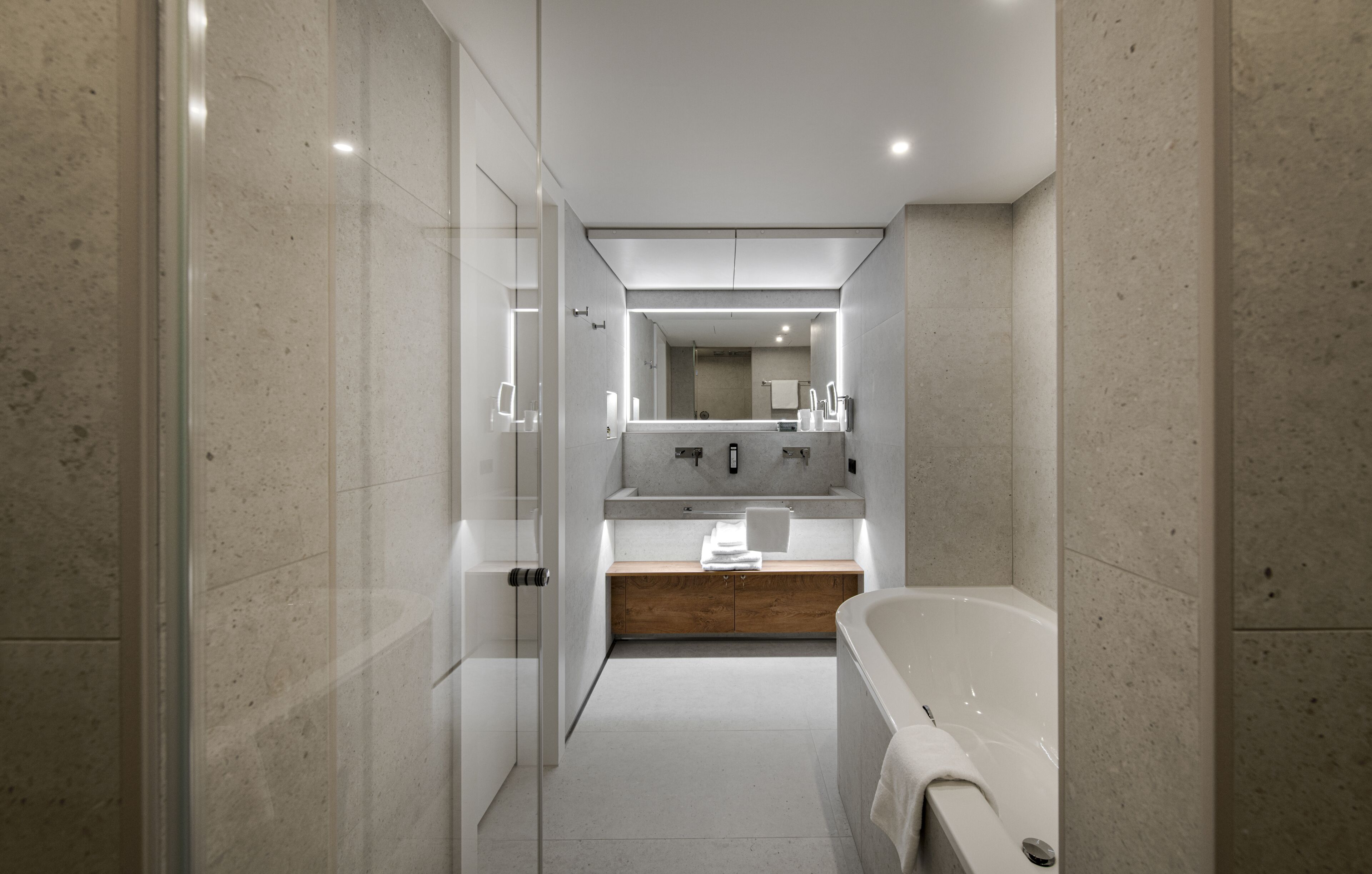 Un baño moderno con cabina de ducha de vidrio, tocador de madera, un espejo grande y una bañera independiente.