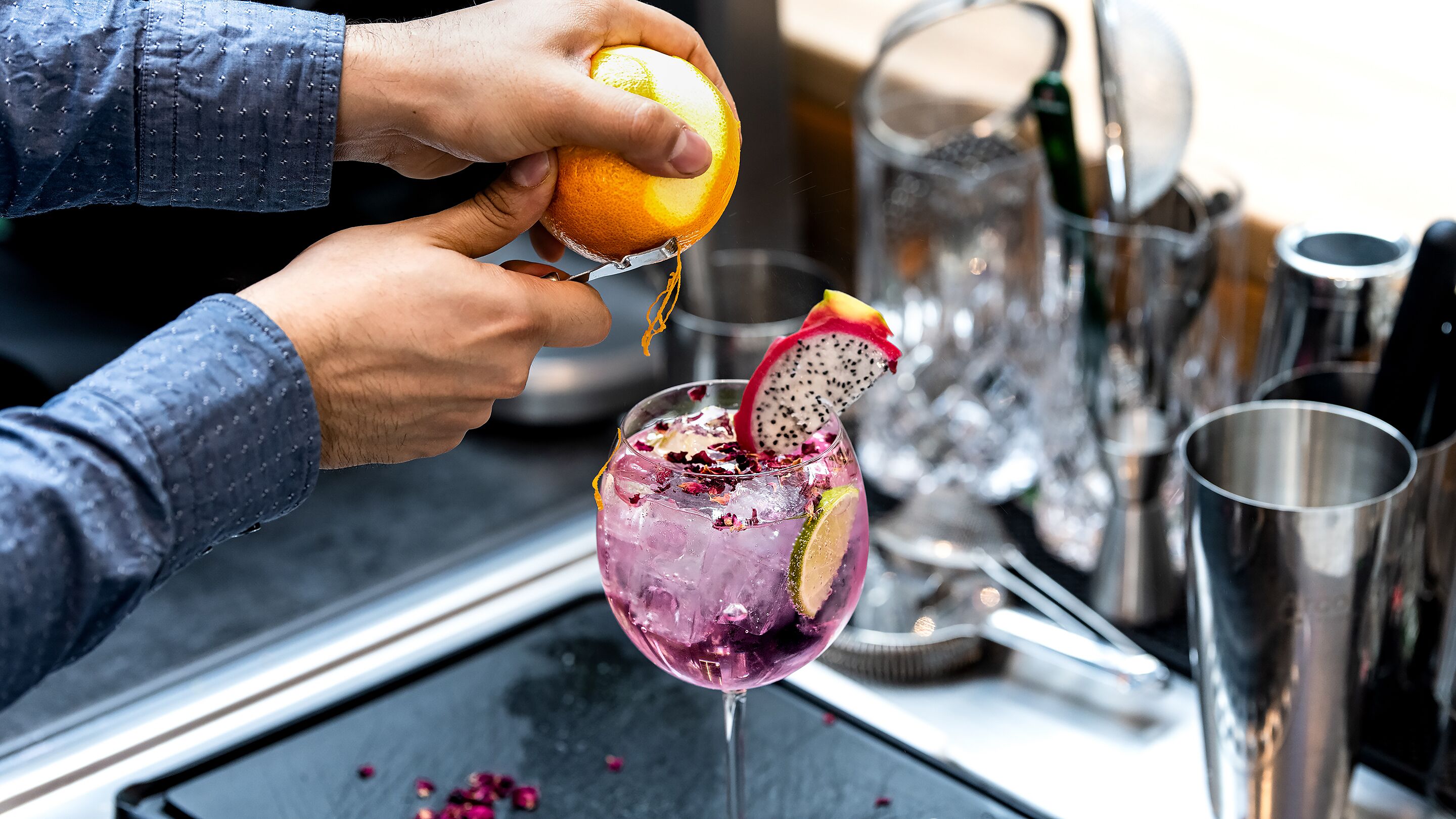Eine Person presst eine Orange in ein Cocktailglas mit einer Drachenfruchtscheibe und Eiswürfeln.
