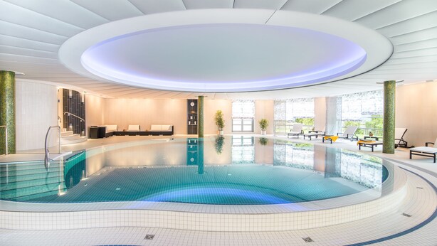 Una piscina interior moderna con diseño circular, rodeada de zonas de descanso y un spa.