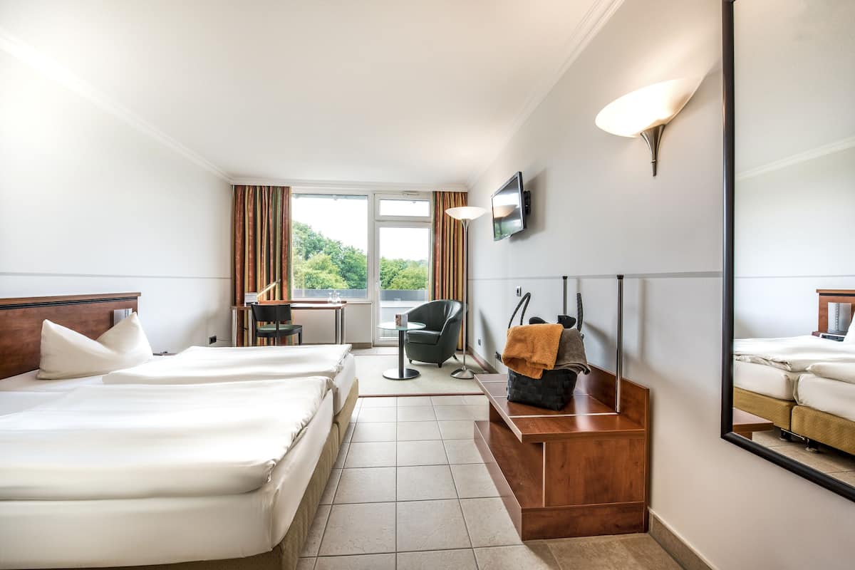 Habitación de hotel con dos camas, un escritorio, una silla, un televisor y un espejo grande.