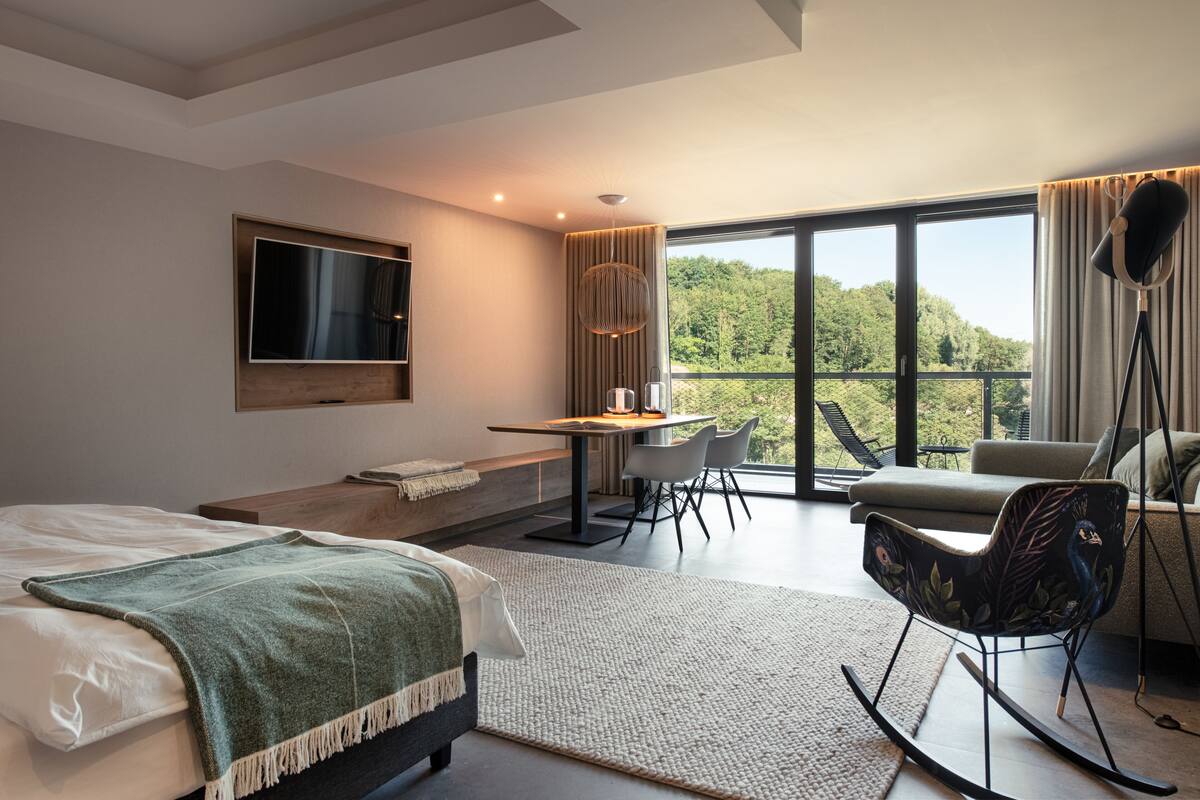 Una habitación de hotel moderna con una cama grande, un escritorio, una mecedora y vistas al exterior.