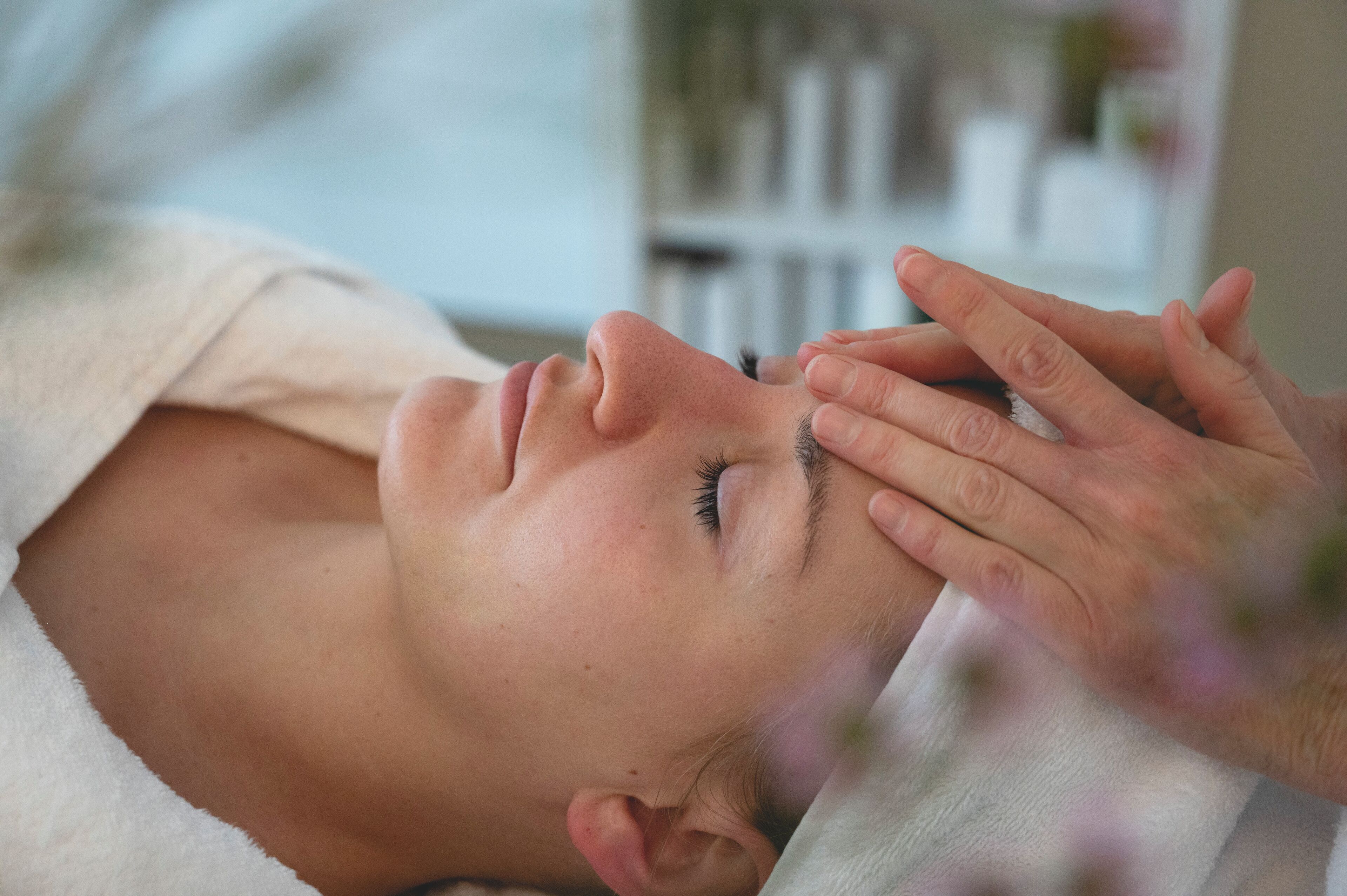 A person lying down with a towel, receiving a facial treatment.