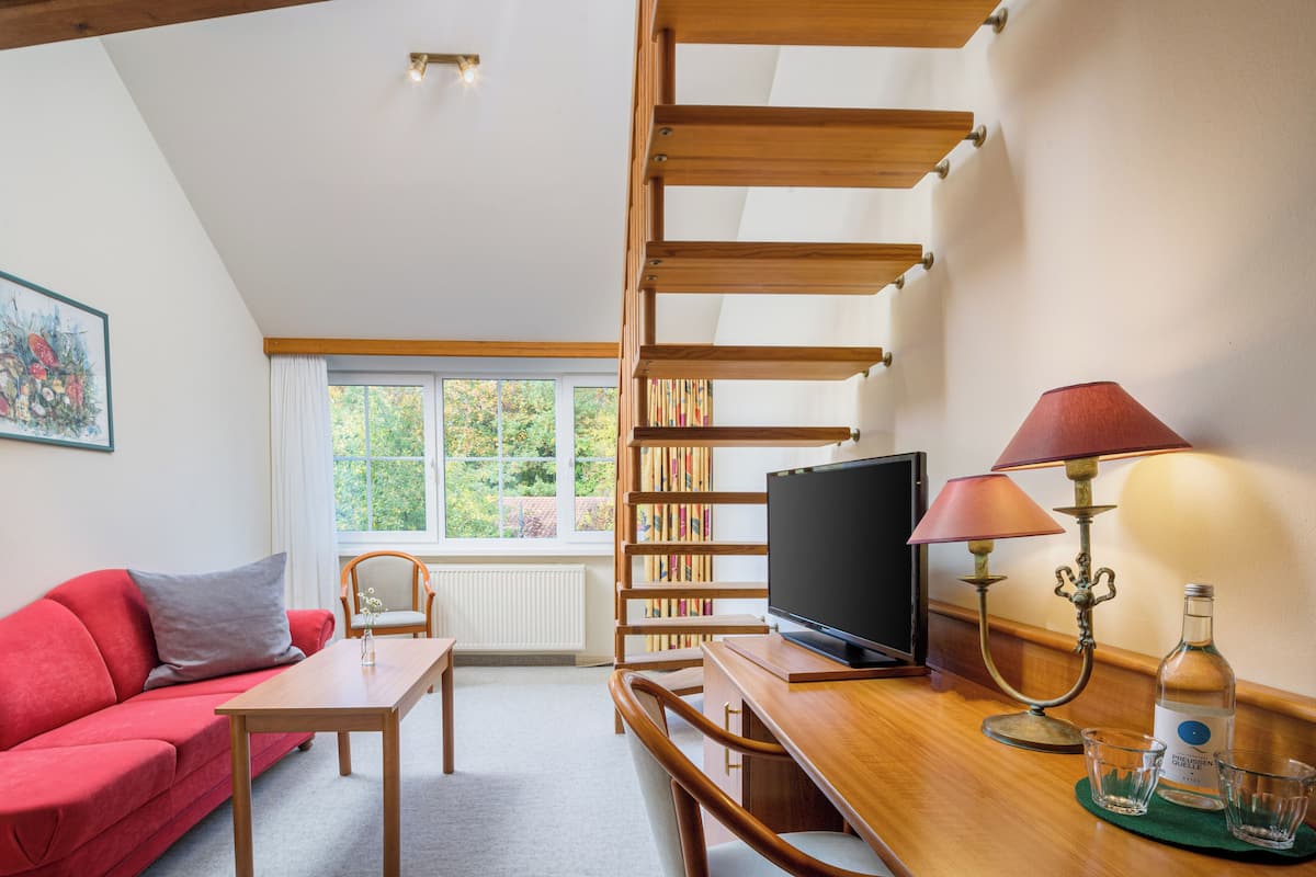 Une pièce chaleureuse avec un canapé rouge, un bureau en bois, une télévision, une lampe et une bibliothèque.