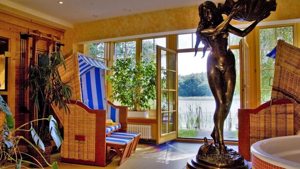 Una habitación con un ventanal grande, una estatua, muebles de mimbre y una bañera.
