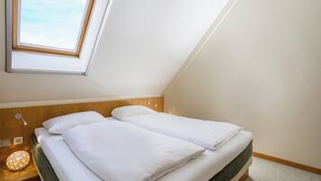 Ein Doppelbett mit weißer Bettwäsche in einem Zimmer mit schrägem Dach und Dachfenster.