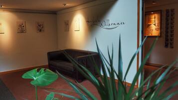 A room with a dark leather sofa, a green plant, and a wall with a welcome sign.