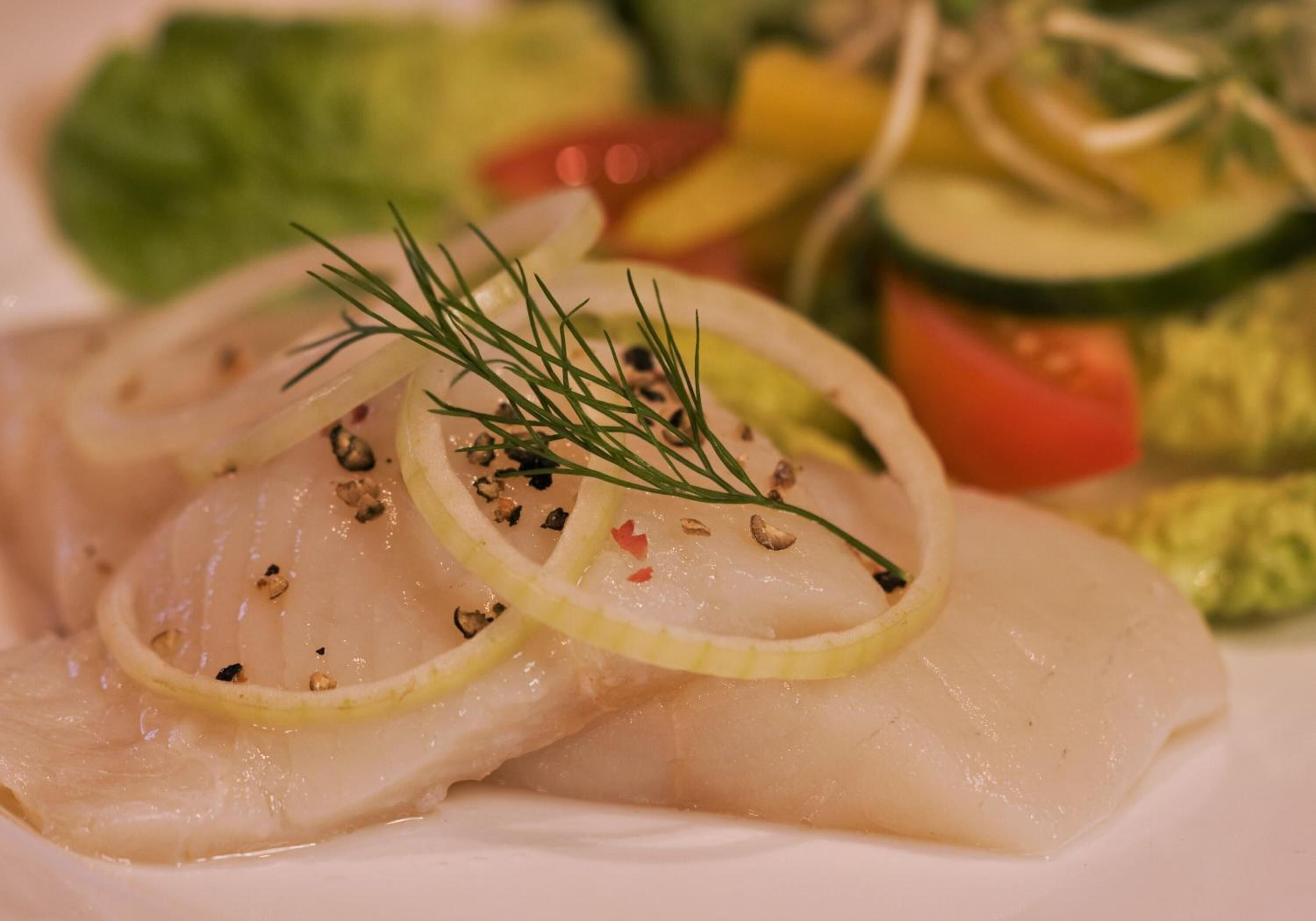 A plate of food with fish, lemon slices, dill, and black pepper.