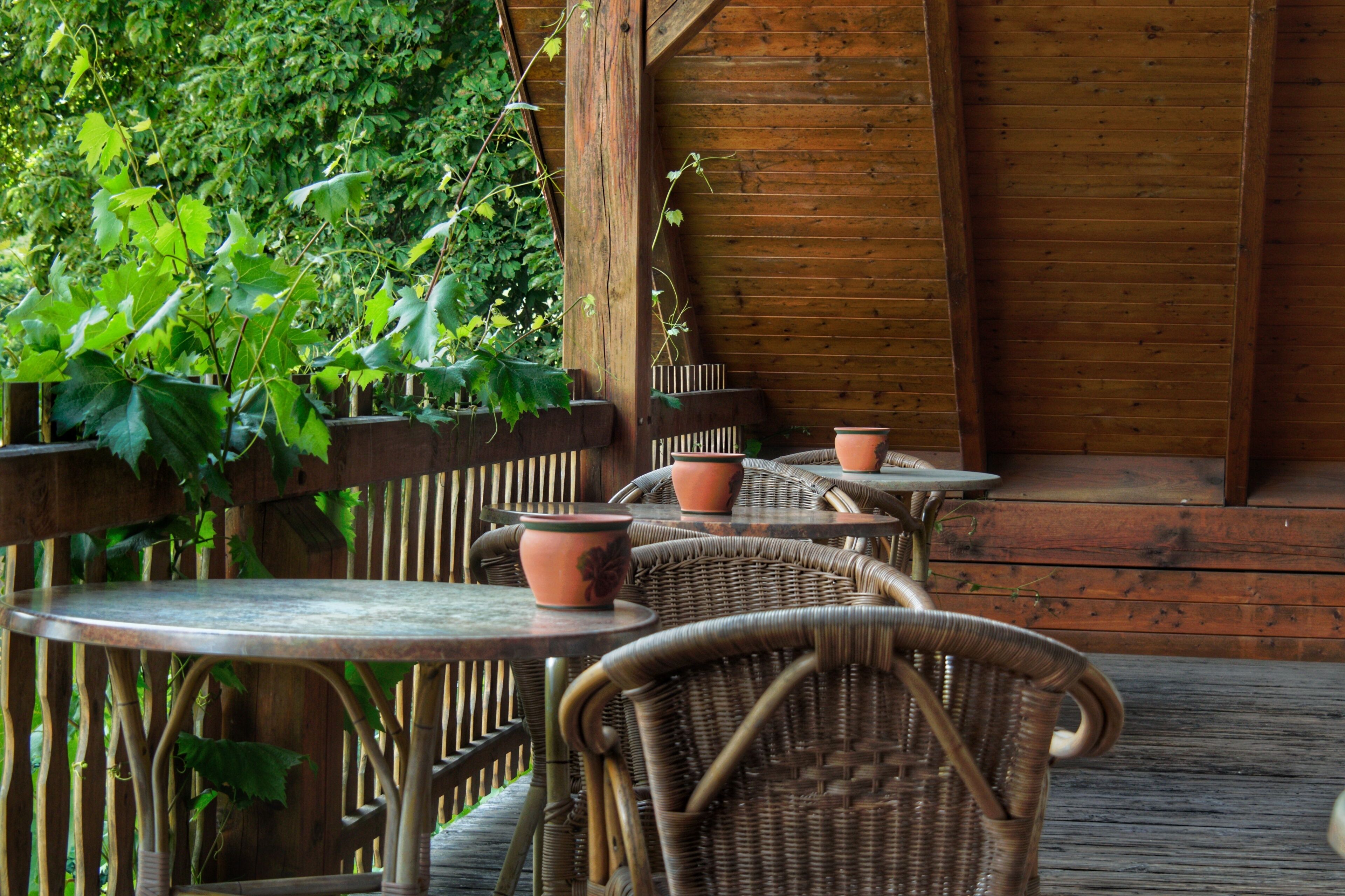 Une terrasse en bois, agrémentée de chaises en osier et de pots en terre cuite, entourée d’une végétation luxuriante.