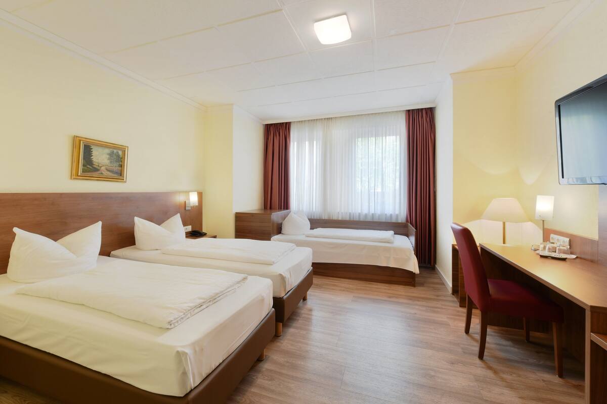 A hotel room with two single beds, a desk, a chair, a TV, and a window with curtains.