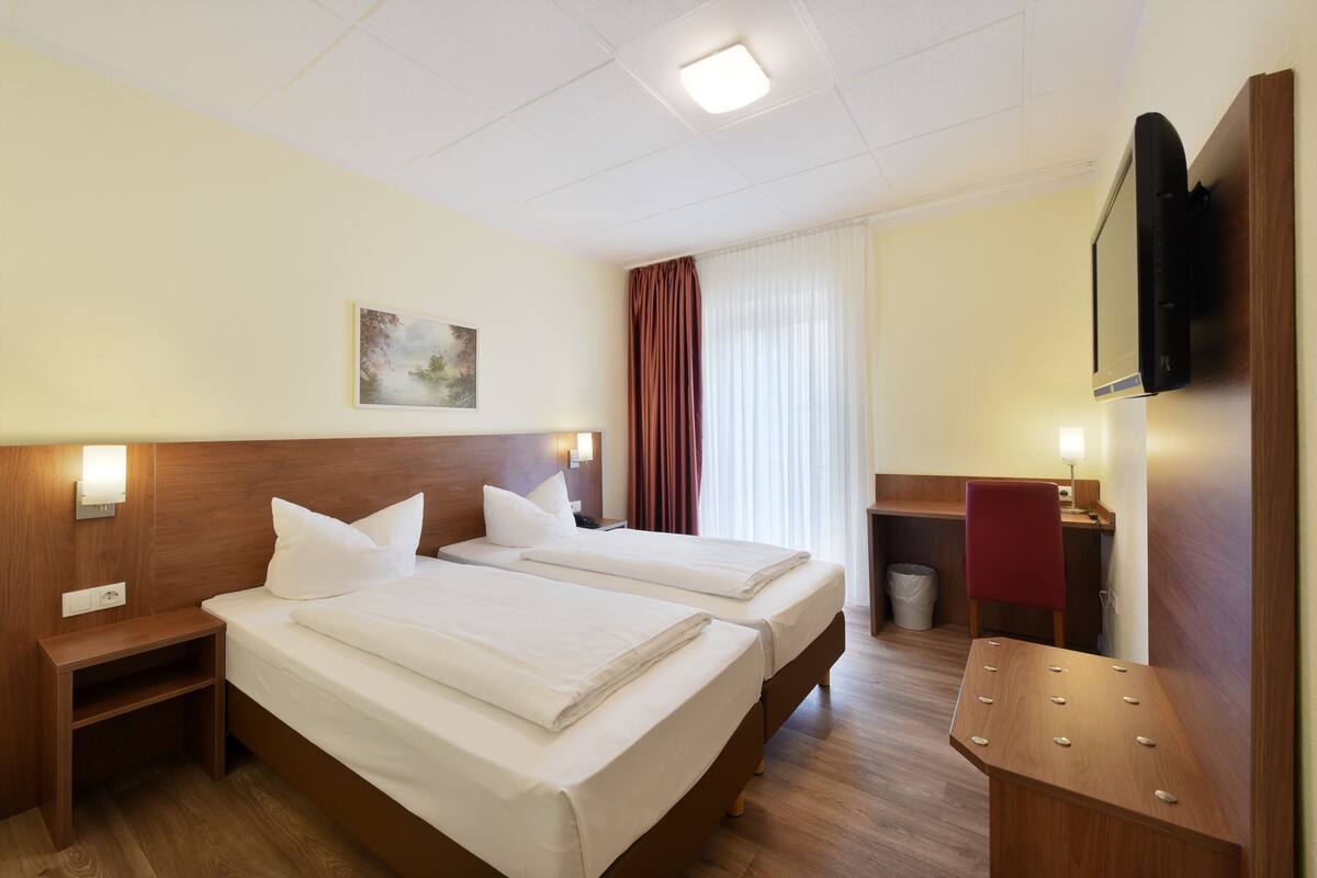 A hotel room with two beds, a desk, a chair, a TV, and a painting on the wall.