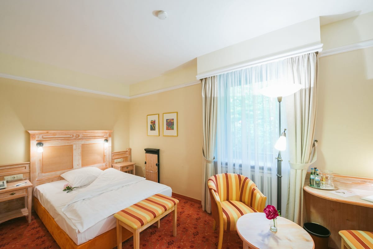 A hotel room with a bed, a desk, a chair, a small table, and a lamp.