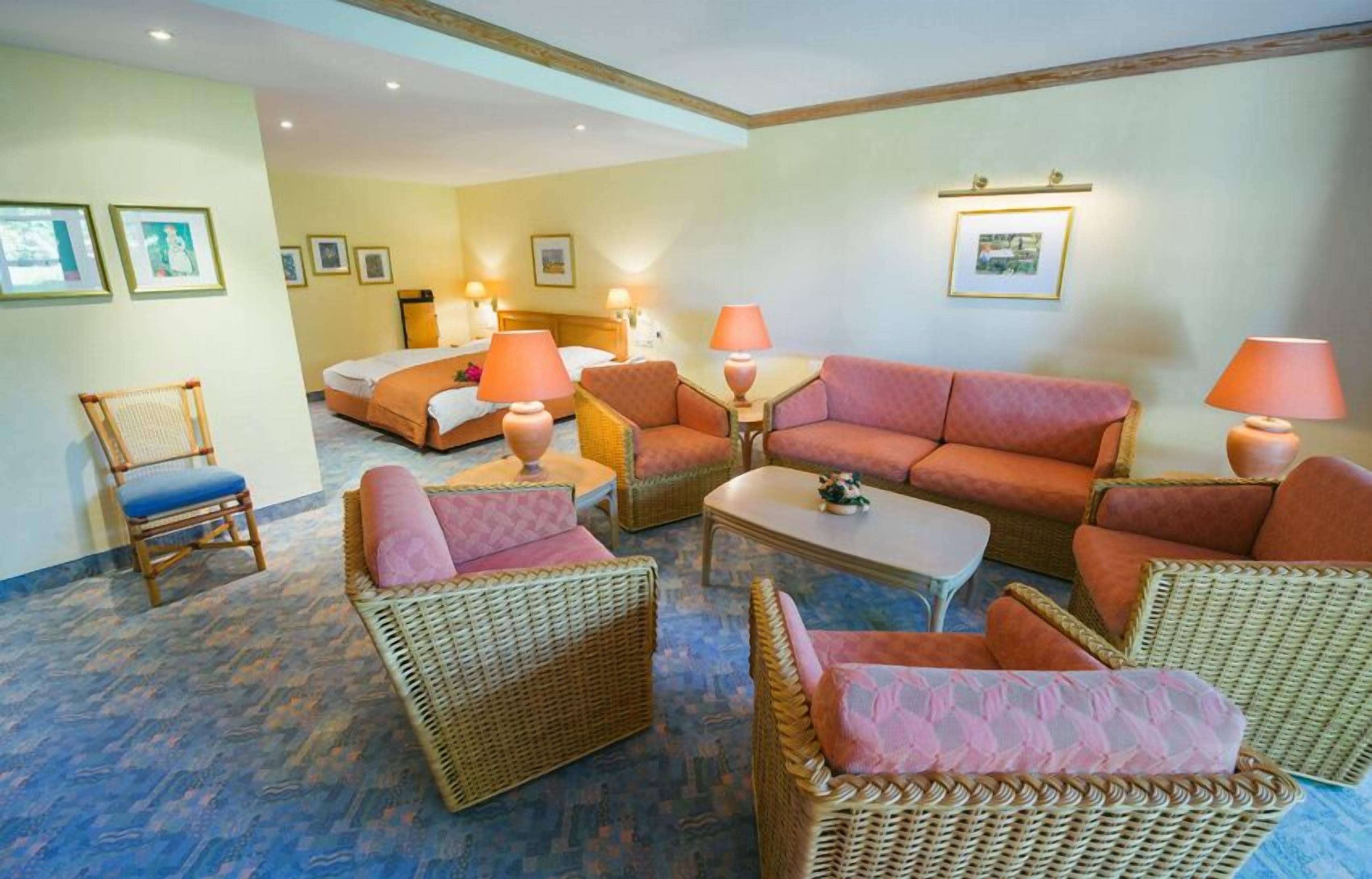 Une chambre d’hôtel comprenant un lit, deux canapés, une table basse et des fauteuils en osier.
