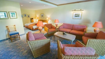 Une chambre d’hôtel comprenant un lit, deux canapés, une table basse et des fauteuils en osier.