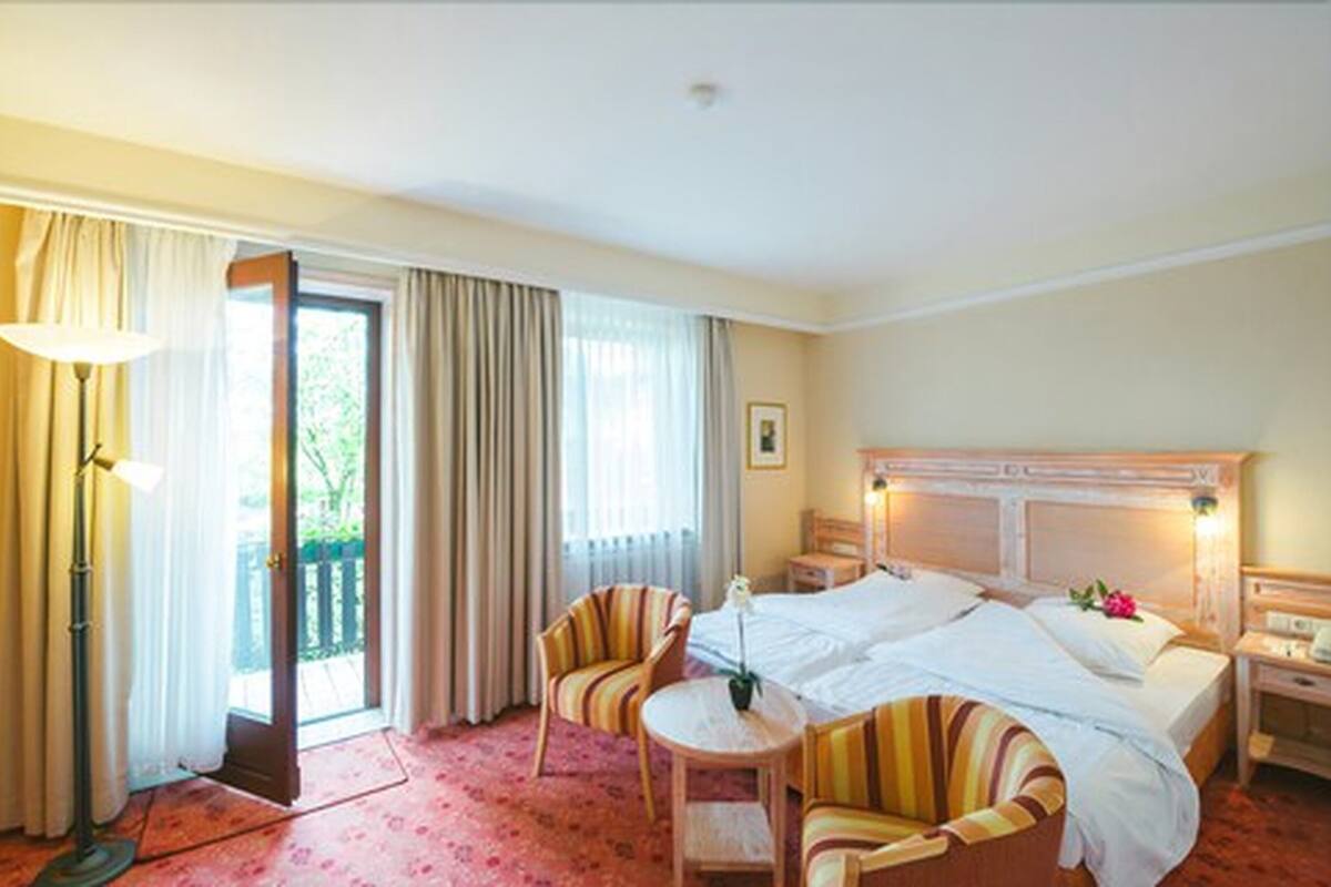 A hotel room with a large bed, two bedside tables, a chair, a lamp, and a view of the outdoors through a sliding door.