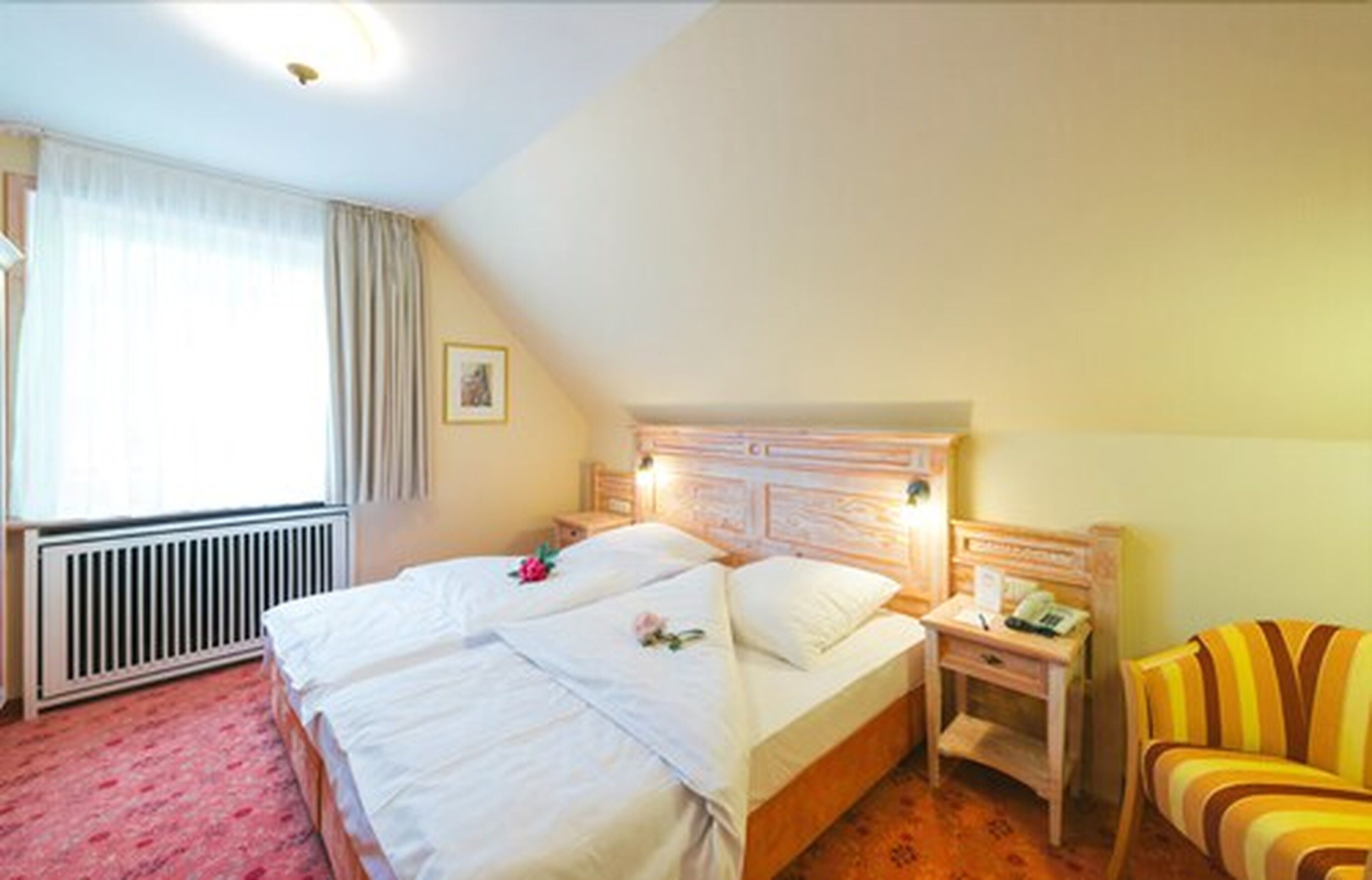 A hotel room with a double bed, a bedside table with a lamp, a chair, and a radiator.
