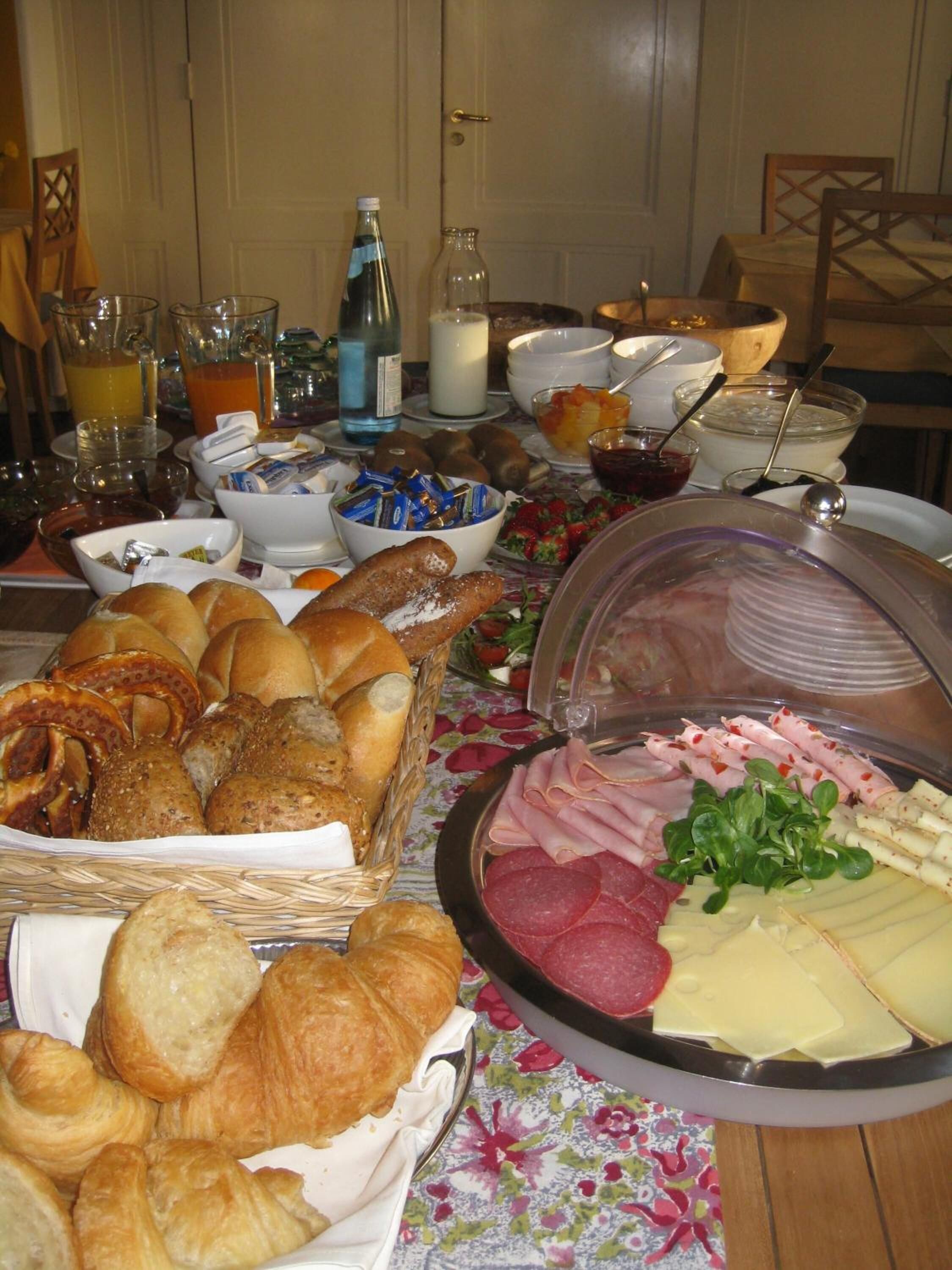 Una mesa de buffet con diversos alimentos, como pan, bollería, carnes y quesos.