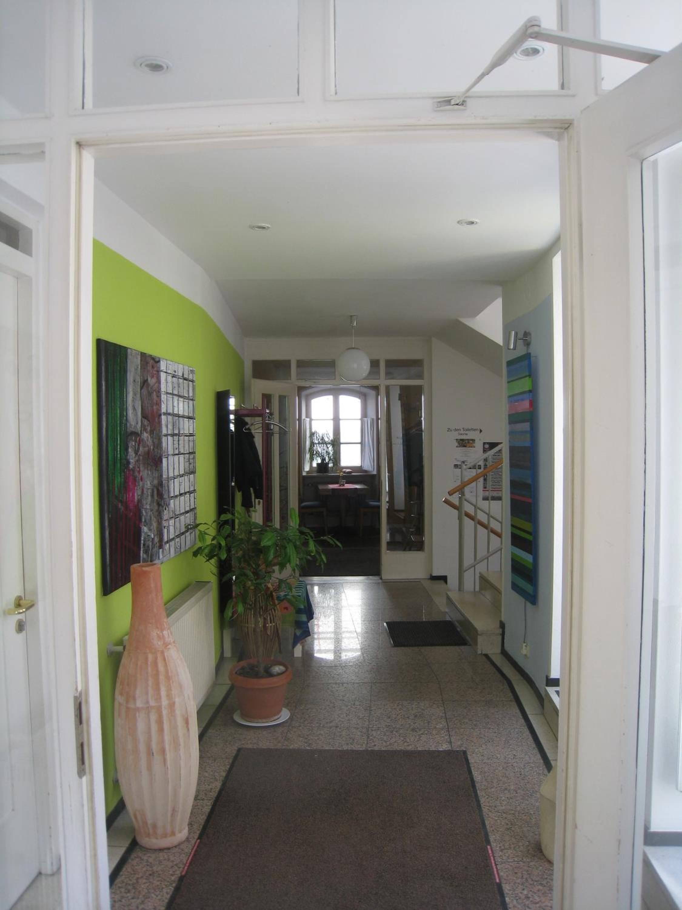 Un couloir avec un mur vert, un grand vase et une plante en pot.
