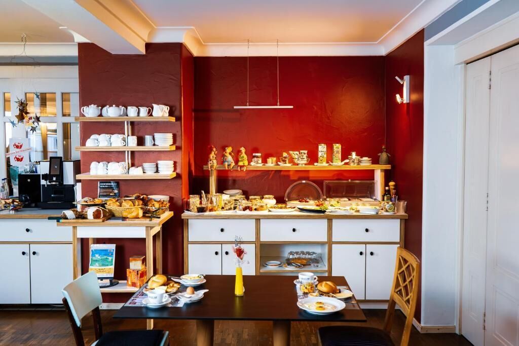 A dining area with a wooden table set for breakfast, surrounded by white cabinets with shelves of dishes and a coffee machine.