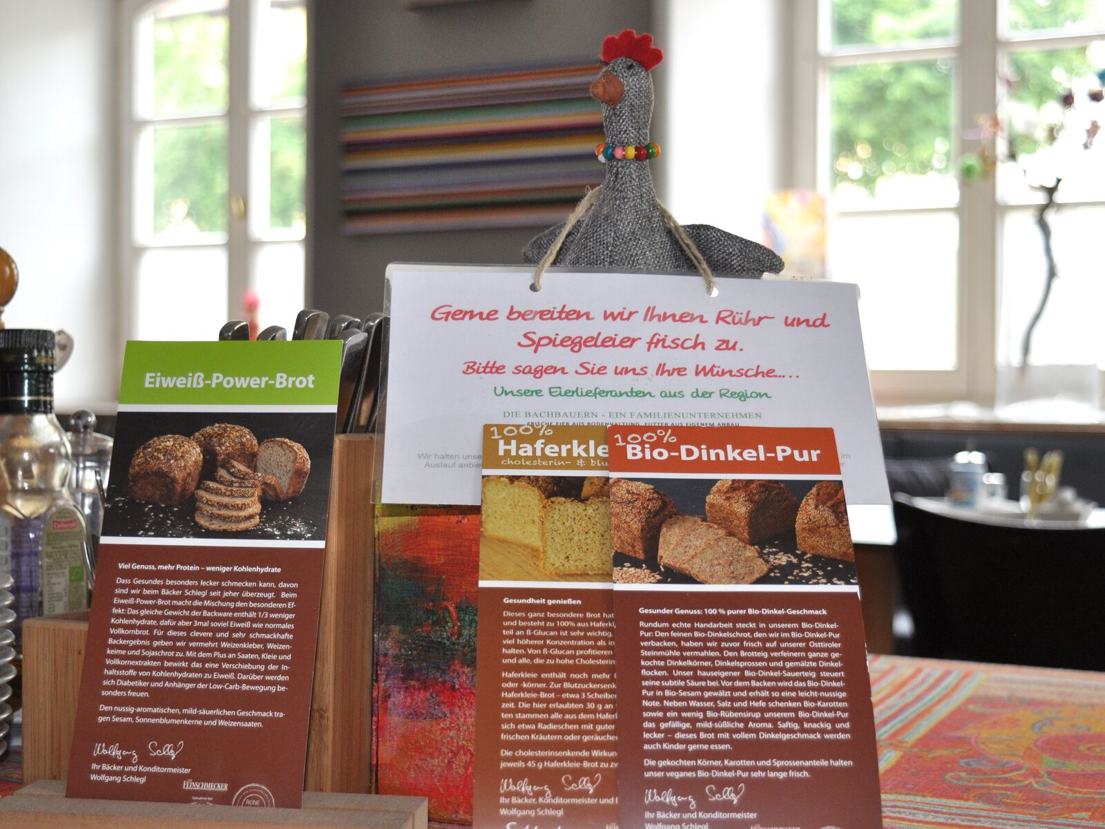 Exhibición de productos alimenticios con descripciones en alemán, incluyendo 'Eiweiß-Power-Brot' y 'Haferkörle Bio-Dinkel-Pur'.