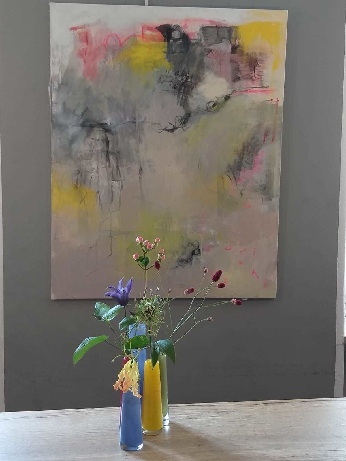 Una pintura con formas y colores abstractos, una mesa con un florero y una pared lisa.