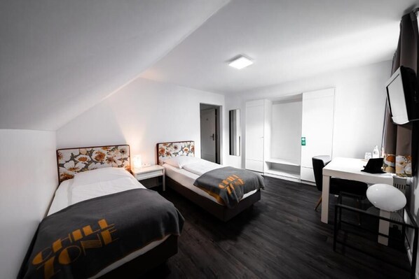 A hotel room with two beds, a desk, and a chair. - Hotel Bergbauer (Neuburg)