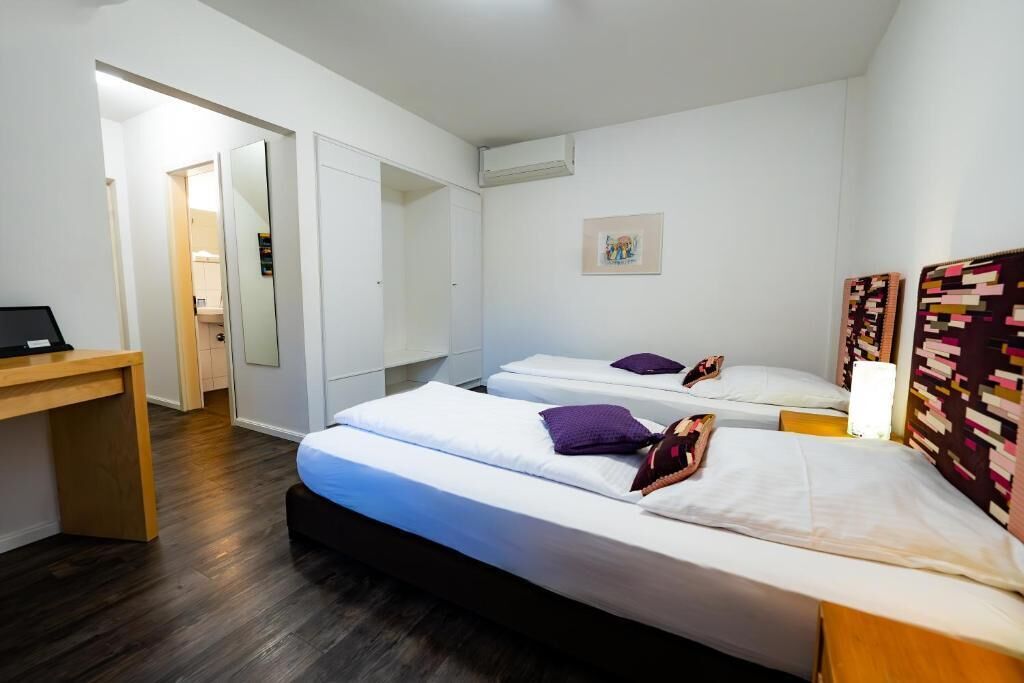 A hotel room with two beds, a desk, and a wardrobe.