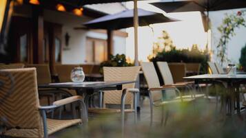 An outdoor seating area with wicker chairs and tables, umbrellas providing shade, and a glass table with a clear glass.