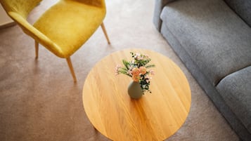 Ein runder Holztisch mit Blumen in einer Vase in einem Raum mit einem grauen Sofa und einem gelben Sessel.