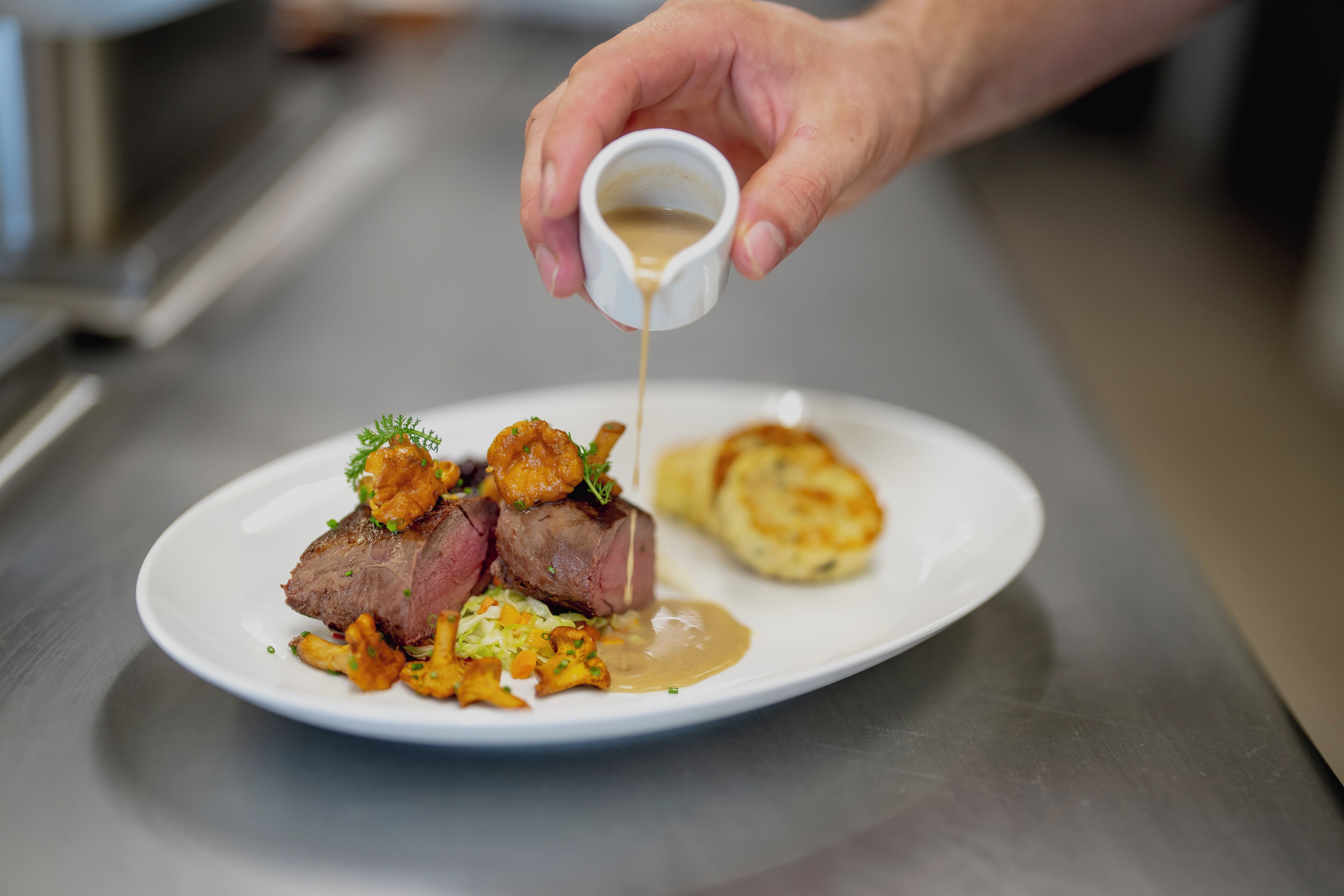 A chef pouring sauce over a dish of meat and vegetables.