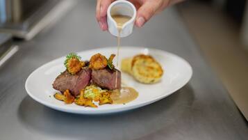 A chef pouring sauce over a dish of meat and vegetables.