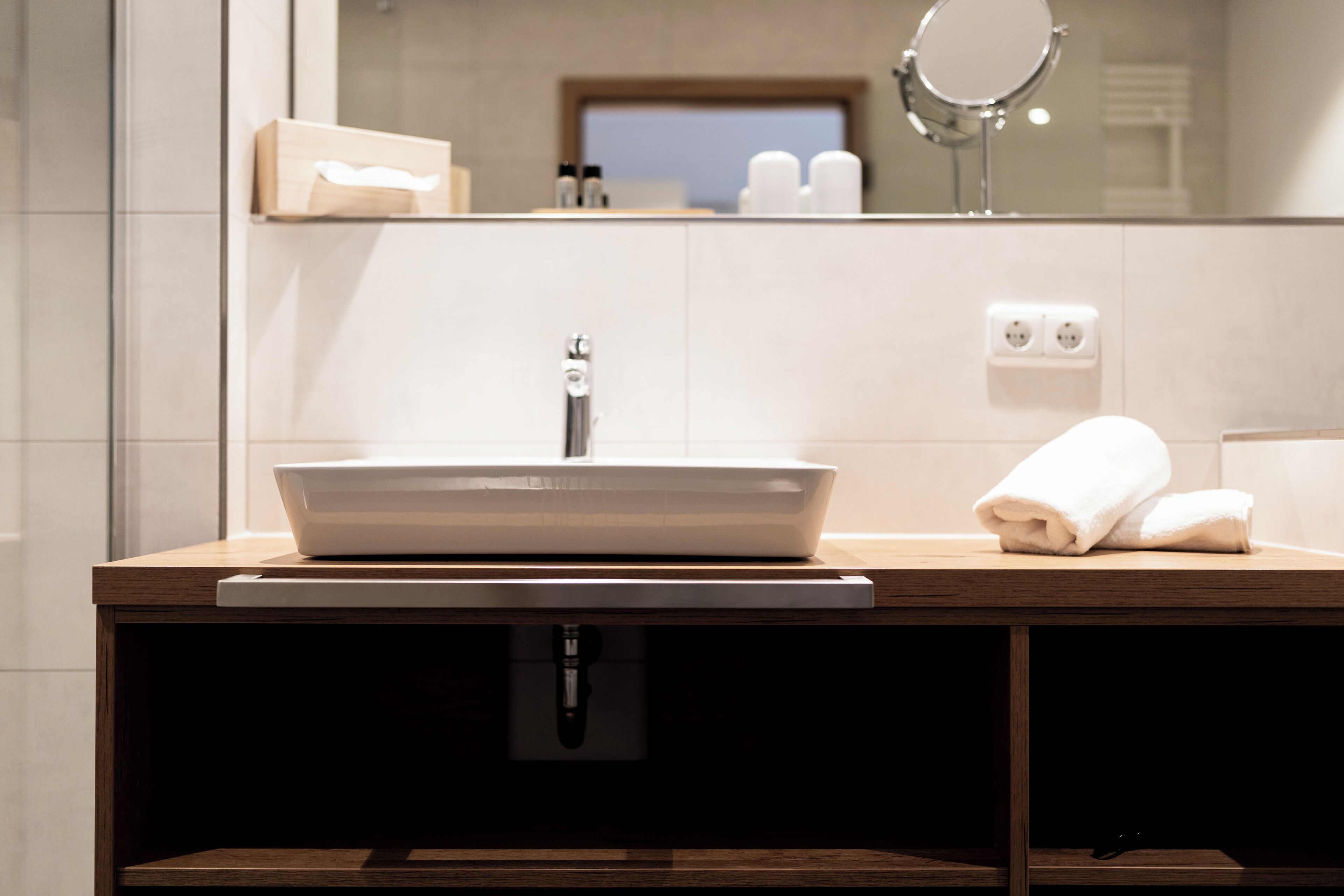 Ein modernes Badezimmer mit einem Holzlager, einem weißen Waschbecken und einem Spiegel darüber.