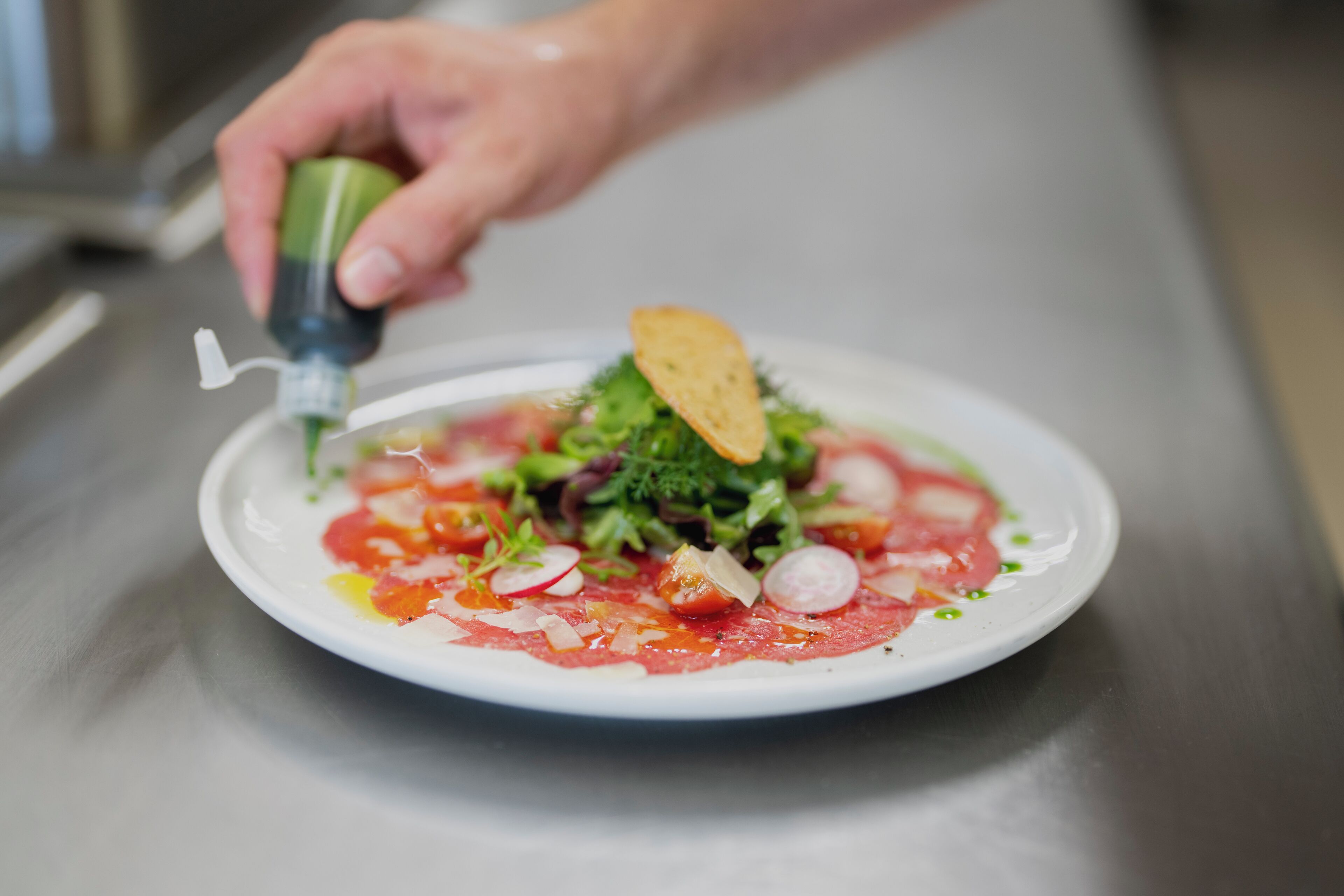 A chef's hand adding a garnish to a dish on a white plate.