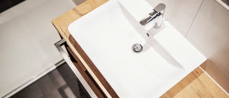 Un baño con lavamanos blanco, encimera de madera y grifo moderno.