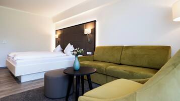 Ein modernes Hotelzimmer mit einem Bett, einer Couch, einem kleinen Tisch mit einer Vase und einem runden Hocker.
