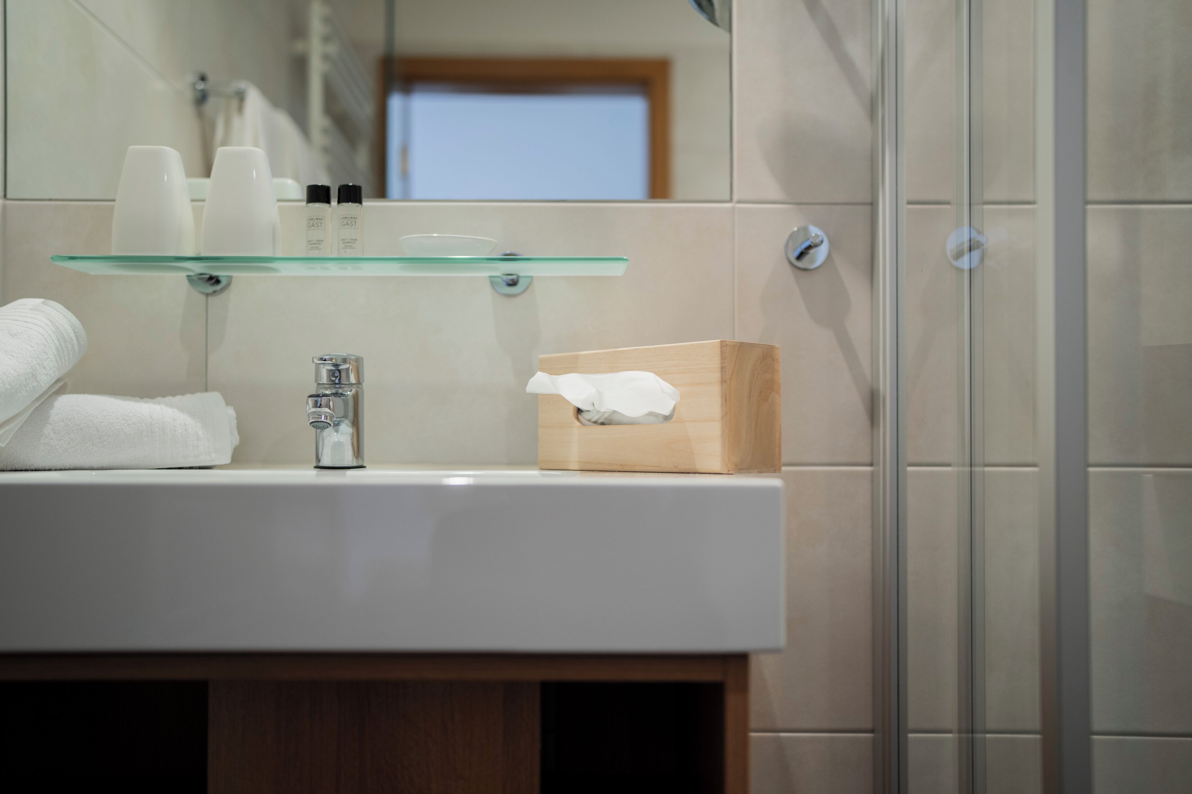 A bathroom with a glass shelf holding toiletries, a sink with a towel, and a wooden box.
