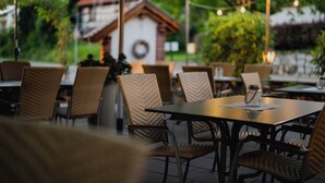 An outdoor dining area with wicker chairs and tables, a small building in the background, and string lights. - Hotel-Gasthof Rose (Oberkirch)