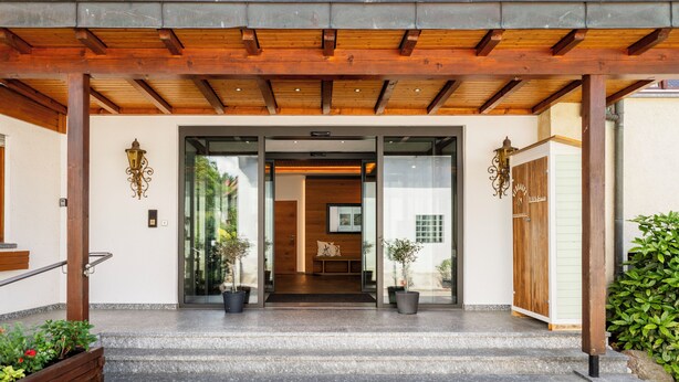 A modern building entrance with a wooden pergola, glass doors, and potted plants. - Hotel-Gasthof Rose (Oberkirch)