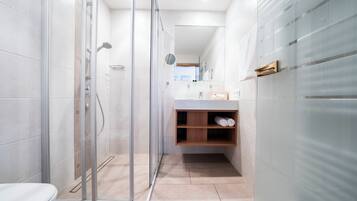 Un baño moderno con cabina de ducha de vidrio, inodoro y tocador con espejo y estantes.
