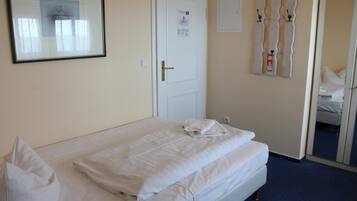 Una habitación de hotel con una cama bien hecha, una puerta con un cartel y un perchero de pared.