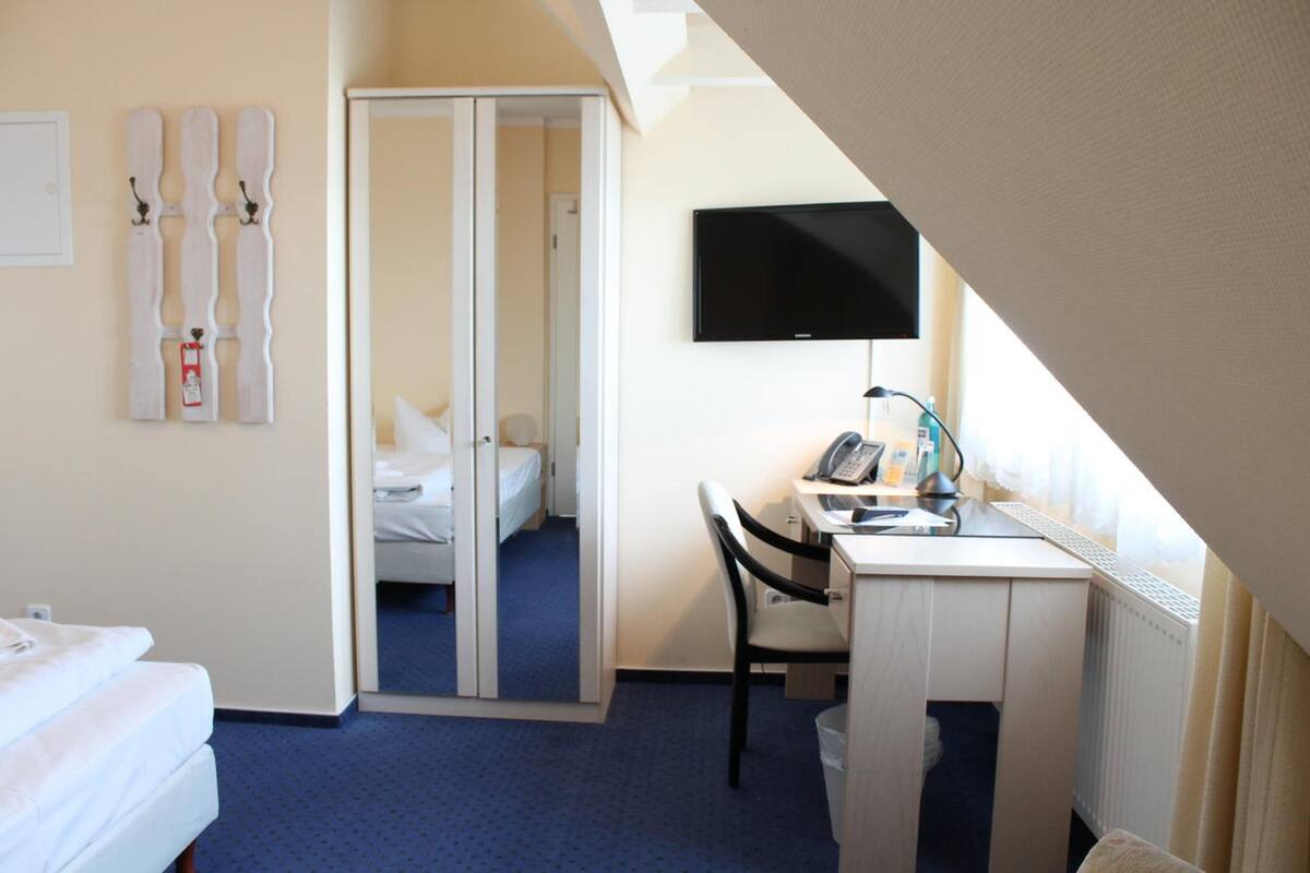 A hotel room with a bed, a desk with a chair, a television, and a closet with a mirror.