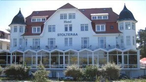 A hotel named 'Hotel Stolteraa' with a large building, a sandy beach, and people relaxing on the beach and in the water. - Hotel Stolteraa (Rostock)